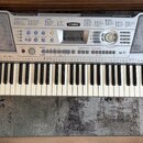 Stříbrný digitální klavír s bílými a černými klávesami. Na horním panelu je v centru logo YAMAHA a vpravo nápis PSR-290. Nástroj obsahuje řadu tlačít…