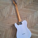 Zadní strana elektrické kytary s bílým korpusem a světle hnědým krčkem z dřeva. Na zadní straně krčku je vidět logo "Fender". Kytara má kovový kryt m…