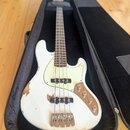 Bílá elektrická basová kytara v černém obalu. Nástroj má světlý hmatník, bílý pickguard a čtyři struny. Povrch bílého trupu vykazuje výrazné opotřebe…