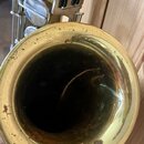 Detailní pohled na čňel mosazného saxofonu. Povrch uvnitř i vně čněle vykazuje výrazné známky opotřebení, oxidaci a tmavé skvrny. V horní části je vi…