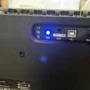 Detail zadní části černého kytarového komba s texturovaným povrchem. V ovládacím panelu jsou vidět konektory AUX, USB a DC IN s nápisem POWER, svítíc…