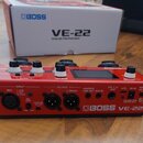 Červený vokální procesor Boss VE-22 s černým šasi a bílými ovládacími knoflíky. Na zadním panelu jsou viditelné nápisy INPUT, MIC, OUTPUT, R, L/MONO,…