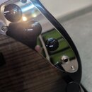 Detailní pohled na tělo elektrické kytary s tmavým dřevěným povrchem a zrcadlovým pickguardem. Na zrcadlovém povrchu jsou vidět tři černé oválné knof…