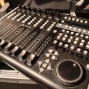 Černá kontrolní plocha s posuvníky, tlačítky a ovládacím knoflíkem. Na zařízení jsou nápisy UNIVERSAL CONTROL SURFACE, X-TOUCH a logo behringer. Povr…