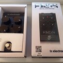 Fotografie zobrazuje kytarový efekt v bílé krabici a vedle ní jeho originální obal. Na zařízení i na krabici je uveden nápis tc electronic a model FA…