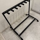 Černý kovový stojan na více kytar s osmi držáky v horní části. Konstrukce tvoří obdélníkový rám s dvěma podnožními tyčemi. Povrch je v matném černém…