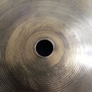Detailní pohled na střed kovového činele zlatavé barvy. Povrch vykazuje koncentrické drážky a drobné škrábance. Na fotografii nejsou žádné viditelné…