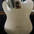Zadní strana elektrické kytary v krémové barvě. Na kovém spojovacím plechu u krku je vyryto logo Squier. V dolní části těla je vidět řada sedmi malýc…