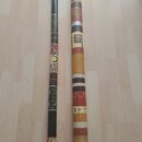 Dvě didgeridou z dřeva s různým povrchovým zdobením. Levý nástroj je tmavě hnědý s barevnými ornamenty a vzory. Pravý nástroj je světlejší, zdobený h…