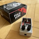 Bílý efekt pedál s nápisy electro-harmonix a PITCH FORK. Na horní straně jsou dva černé ovládací knoflíky, červený spínač a přepínač s označením LATC…
