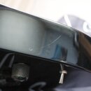 Detailní pohled na černý, lesklý povrch hudebního nástroje. Na hraně jsou vidět drobné škrábance a oděrky. V dolní části je viditelný kovový knurlova…