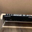 Černý elektronický nástroj s nápisy „elektron“ a „Analog Rytm MKII“. Na zadním panelu jsou umístěny různé konektory a popisky, včetně „Power“, „12VDC…