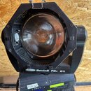 Černý svítící reflektor s kulatým sklem a kovovým vnitřním odrazem. Na spodní hraně těla je bílý nápis „ShowTec Moving Par 64“. V dolní části jsou vi…