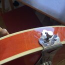 Detailní pohled na spodní část trupu elektrické kytary v červenohnědé barvě s krémovým bindingem. Je vidět chromovaný stop-bar most a kotva strun s k…