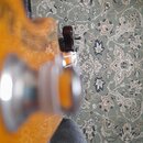 Detailní pohled na část těla kytary v žluté barvě s viditnou strukturou dřeva. Na povrchu je umístěn stříbrný kovový knofík s průhledným vrchem. Foto…