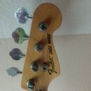 Fotografie zachycuje hlavu basové kytary z přírodního dřeva se čtyřmi chromovanými ladičkami. Na povrchu je černý nápis Fender Jazz Bass. Povrch dřev…