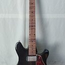 Černá elektrická kytara s tmavě hnědým hnedem hmatníkem a dřevěnou hlavou. Na hlavě je viditelné logo "Cort". Kytara má dva humbuckery, červeně vzoro…