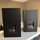 Dva černé regálové reproduktory z pohledu zezadu. Na zadní straně každého reproduktoru je štítek s nápisy KEF Q10 SP3168, IMP 6Ω a 10-100W. Levý repr…