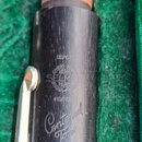 Detailní pohled na horní část černého dřevěného klarnetu v zeleném pouzdře. Na nástroji je vyryto „DEPOSE“, logo s nápisem „HENRI SELMER PARIS“, slov…