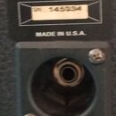 Detail zadní strany zařízení s jedním zapuštěným jack konektorem. Nad konektorem je nápis 4 OHMS a MADE IN U.S.A. Mezi nimi se nachází štítek s označ…