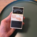 Bílý efekt pedál s černým spínacím pedálem a analogovým ukazatelem v horní části. Na zařízení jsou nápisy BOSS, Chromatic Tuner TU-3 a označení vstup…