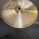 Zlatý mosazný činel umístěný na kovovém stativu. Na povrchu je černý nápis „istanbul“ a pod ním menší text „Mehmet Handmade Cymbals from Turkey“. V l…