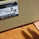 Detail štítku na béžovém textilním povrchu reproduktoru. Na bílém štítku jsou nápisy: "EY CTRONICS RPORATION", "711 A STREET MERIDIAN, MS 39301 USA",…