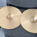 Dvě mosazné činely položené na šedém textilním povrchu. Horní činel má hladký povrch a v pravé dolní části logotyp s nápisem Zildjian. Spodní činel m…