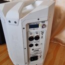 Bílý přenosný reproduktor s integrovanou ovládací sekcí a úchytem v horní části. Na předním panelu jsou nápisy QuickSmartDSP | MONITOR, POWERED BY DY…