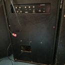 Černý kytarový kombozesilovač s povrchem z textilie. Na ovládacím panelu jsou nápisy VOLUME, BASS, TREBLE, REVERB a logo ME I. Panel obsahuje čtyři o…