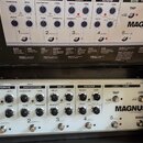 Bílá multifunkční efektová pedálboard s nápisy T-REX a MAGNUS. Zařízení obsahuje několik sekcí označených jako OVERDRIVE, DISTORTION, DELAY a REVERB,…