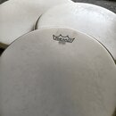 Tři bílé bubnové blány z plastu. Na přední bláně je černé logo REMO a nápis EMPEROR WHITE SLIDE MADE IN U.S.A. Povrchy blán vykazují známky používání…