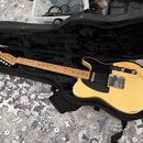 Světle žlutá elektrická kytara typu Telecaster v černém poloměkém pouzdře. Na hlavě hmatníku je viditelné logo Fender. Kytara má javorový krk, černý…