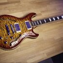 Polodupatá elektrická kytara s vyznačenou strukturou dřeva v žlutohnědé barvě. Nástroj má dva humbuckery s modrými cívkami a krčkem s trapezoidními v…