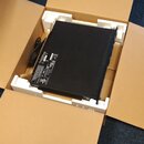 Černý dikdörtníkový elektronický přístroj v originální kartonové krabici s bílými polystyrenovými vložkami. Na zadní straně zařízení je viditelný ští…