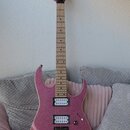Elektrická kytara s růžovým třpytivým povrchem a světlým hnedým hnedým hmatníkem. Na hlavě je viditelný nápis Danelectro. Nástroj má dva snímače typu…