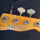 Fotografie zachycuje hlavu basové kytary z přírodního dřeva s viditelným opotřebením povrchu. Na dřevě je umístěno logo Fender a nápis PRECISION BASS…