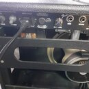 Zátylový panel kytarového komba s černým povrchem a stříbrnými prvky. Jsou zde přepínače POWER a STANDBY, vstup INPUT POWER s připojeným kabelem, poj…