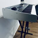 Digitální klavír umístěný na černém X-stojanu. Na stříbrném bočním panelu je vyraženo logo a nápis KETRON. Na horním ovládacím panelu je vidět modrý…