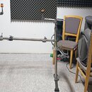 Kovový stojan pro bicí nástroje s dvěma vertikálními nohami a spojovací vodorovnou tyčí. Stojan je stříbrné barvy s černými gumovými koncovkami nožní…