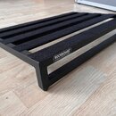 Černý obdélníkový pedalboard z kovového materiálu s mřížkovým vrchem. Horní lišty jsou potaženy černým velkrotextilem. Na boční straně je bílý nápis…