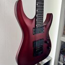 Elektrická kytara s matným povrchem v tmavě červené barvě. Nástroj má dva černá humbuckery a dva ovládací knoflíky. Na těle nejsou vidět žádná loga a…