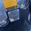 Detailní pohled na kovovou spojovacídesku krku a těla elektrické kytary. Na chromovaném povrchu desky je vyryt nápis Fender. Deska je připevněna čtyř…