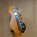 Zadní strana hlavy kytary z přírodního dřeva s šesti chromovanými ladičkami. Na každém ladičce je vyryto logo Fender. Na dřevě je černý nápis MADE IN…