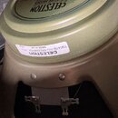 Fotografie zachycuje zadní část reproduktoru v olivově zelené barvě. Na magnetu je vidět bílá nálepka s nápisy CELESTION, T5647B G10 GREENBACK 16 Ω a…
