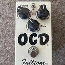 Bílý efekt pedál s nápisy OCD a Fulltone. Na horní části jsou tři černé oválné knoflíky s popisky Volume, Drive (částečně zakrytý) a Tone. Mezi knofl…