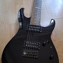 Černá elektrická kytara s tmavým hnedým hmatníkem a dvěma humbuckery. Na hmatníku je viditelný nápis CORE. Tělo kytary vykazuje drobné oděrky a prach…