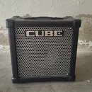 Černý kytarový kombozesilovač s kovovou mřížkou reproduktoru. Na horní části mřížky je bílý nápis CUBE. Nástroj má v horní části přenosnou rukojeť a…