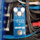 Modrý efekt pedál s nápisy „mini EGO Compressor“ a „WAMPLER BUILT IN USA“. Na horní straně jsou tři bílé oválné knoflíky s popisky „TONE“, „VOLUME“ a…