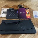 Sada příslušenství pro kytaru položená na dřevěné podlaze. Obsahuje tři balení strun značek Ernie Ball (nápisy Acoustic Bronze, HAB0944), D'Addario (…